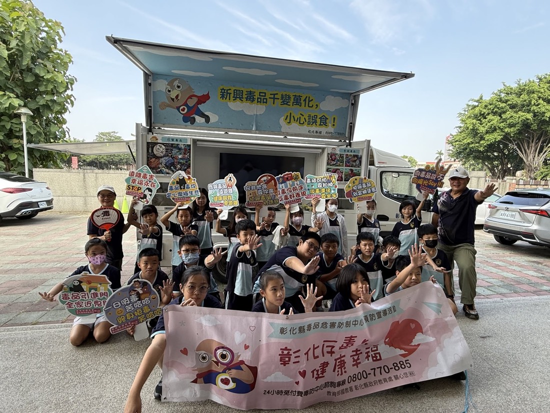 五年級學生在反毒教育行動車前舉牌合影 · Fifth-graders pose with pledge cards in front of the anti-drug education truck