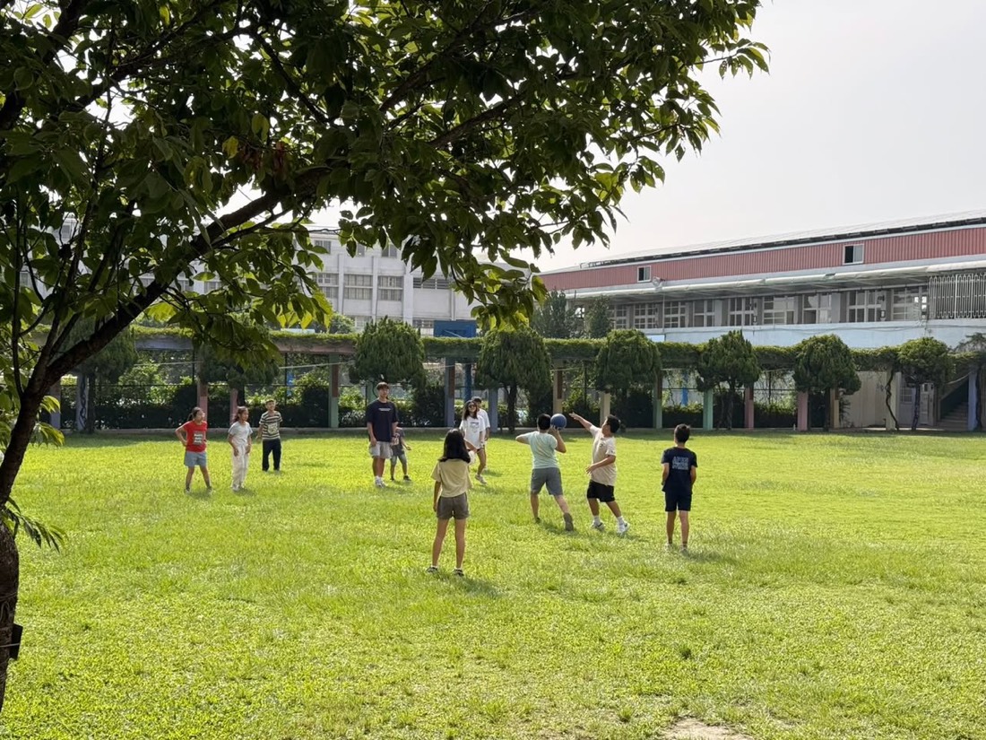 孩子與大專青年志工在草地上活動筋骨 · Children and college volunteers stretch and play on the lawn