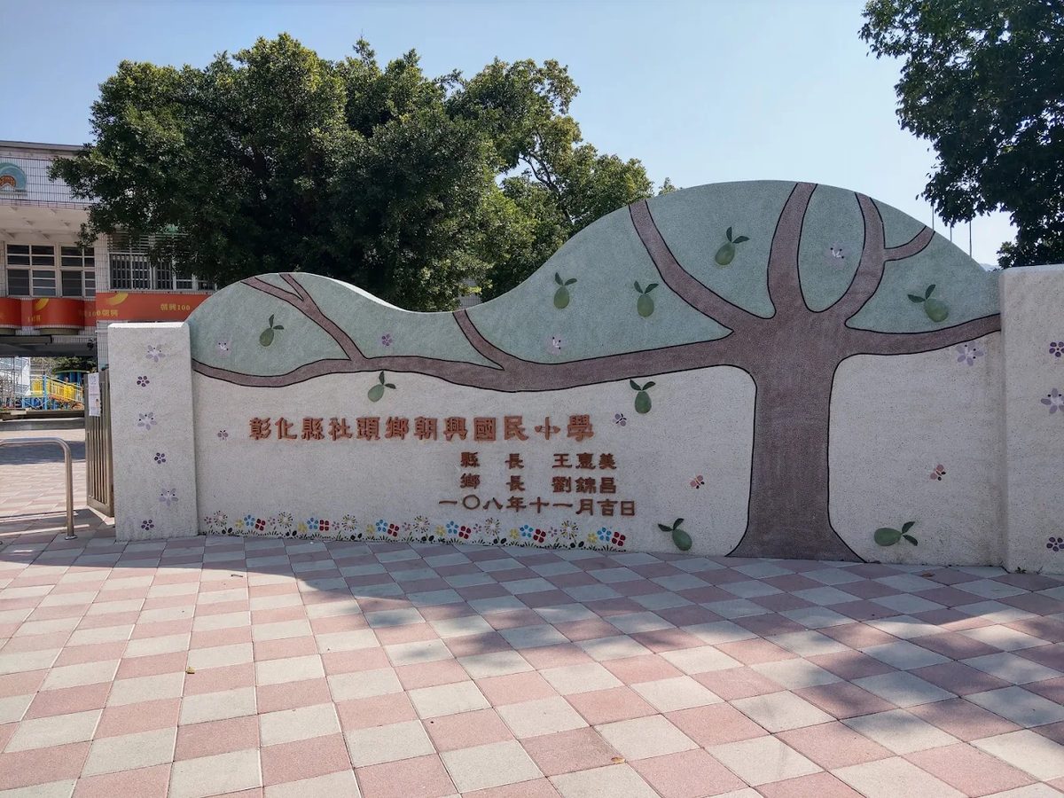 朝興國小校門的低矮弧形圍牆,浮雕一棵結著芭樂的大樹,牆上刻著「彰化縣社頭鄉朝興國民小學」 The low curved wall at the Chaohsing gate, with a relief of a large tree bearing guava and the school’s carved name