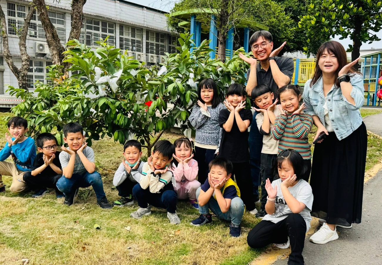朝興國小學生與校長、老師在校園的芭樂樹前合影，比出手托腮的可愛姿勢 Chaohsing children with the principal and a teacher in front of a campus guava tree