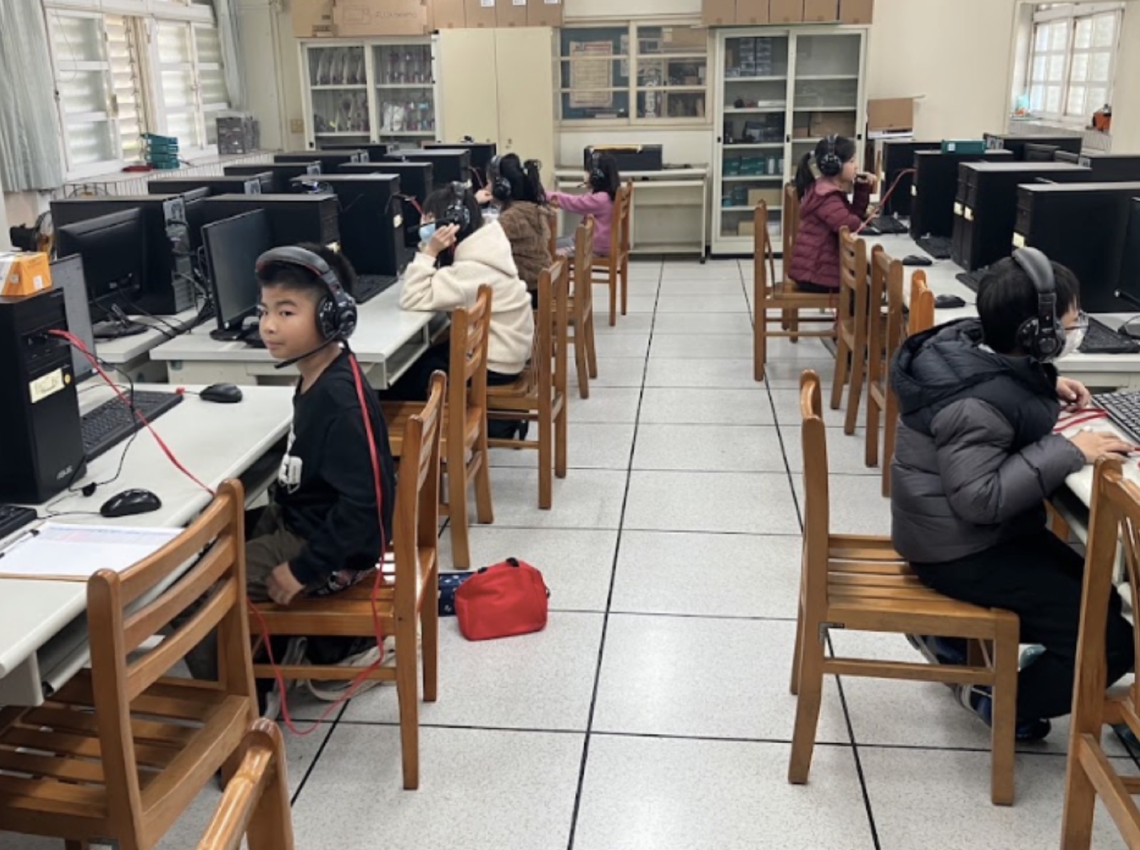 學生們戴著耳機在電腦教室進行遠距雙語課程