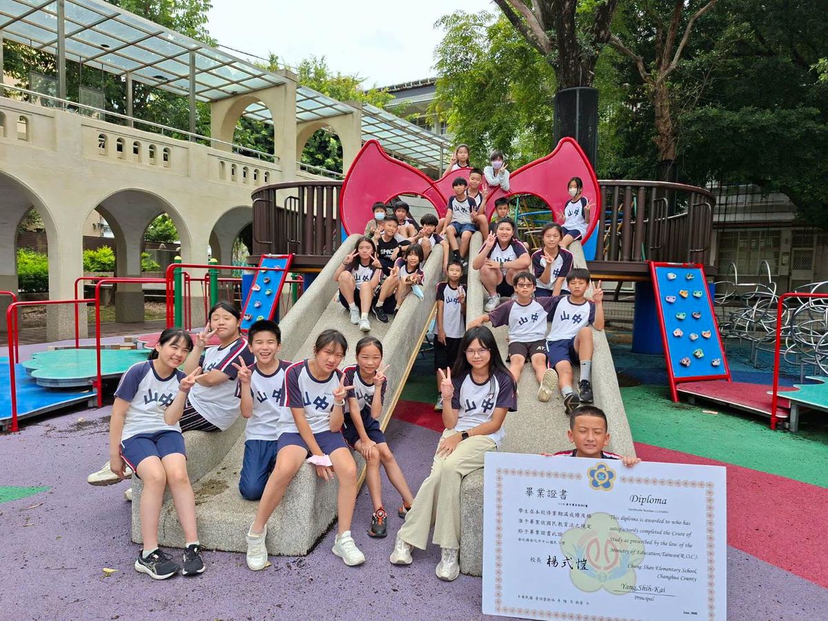畢業生在遊戲場滑梯前開心合影，手持畢業證書