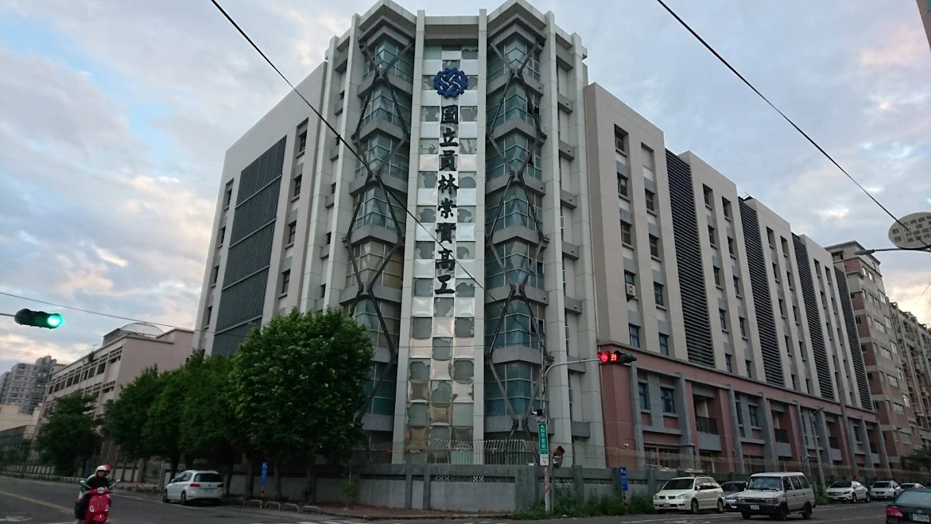 崇實高工臨街的高樓立面，中央直書「國立員林崇實高工」，上方是藍色齒輪校徽 The street-facing tower at ChungShih, the school's name set vertically down the façade beneath the blue gear crest