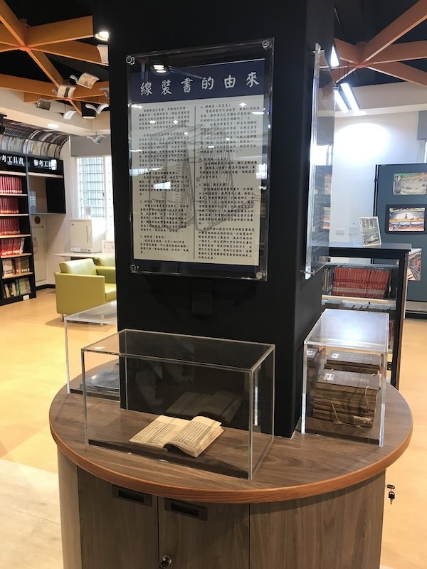 展櫃中攤開展示的線裝書，上方海報說明線裝書的由來 A thread-bound book lying open in the display case, the poster above explaining where such books came from