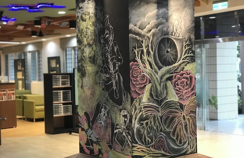 柱子上由學生以粉筆彩繪的黑板漆作品，畫著花卉、齒輪與人物 A pillar covered in chalkboard paint and painted by a student artist with flowers, a gear and figures