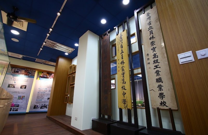 常設展區的校史展示牆，掛著早年「臺灣省立員林崇實高級工業職業學校」的木質校牌 The permanent school-history display, with the school's old wooden name board from its provincial-era title hanging on the wall