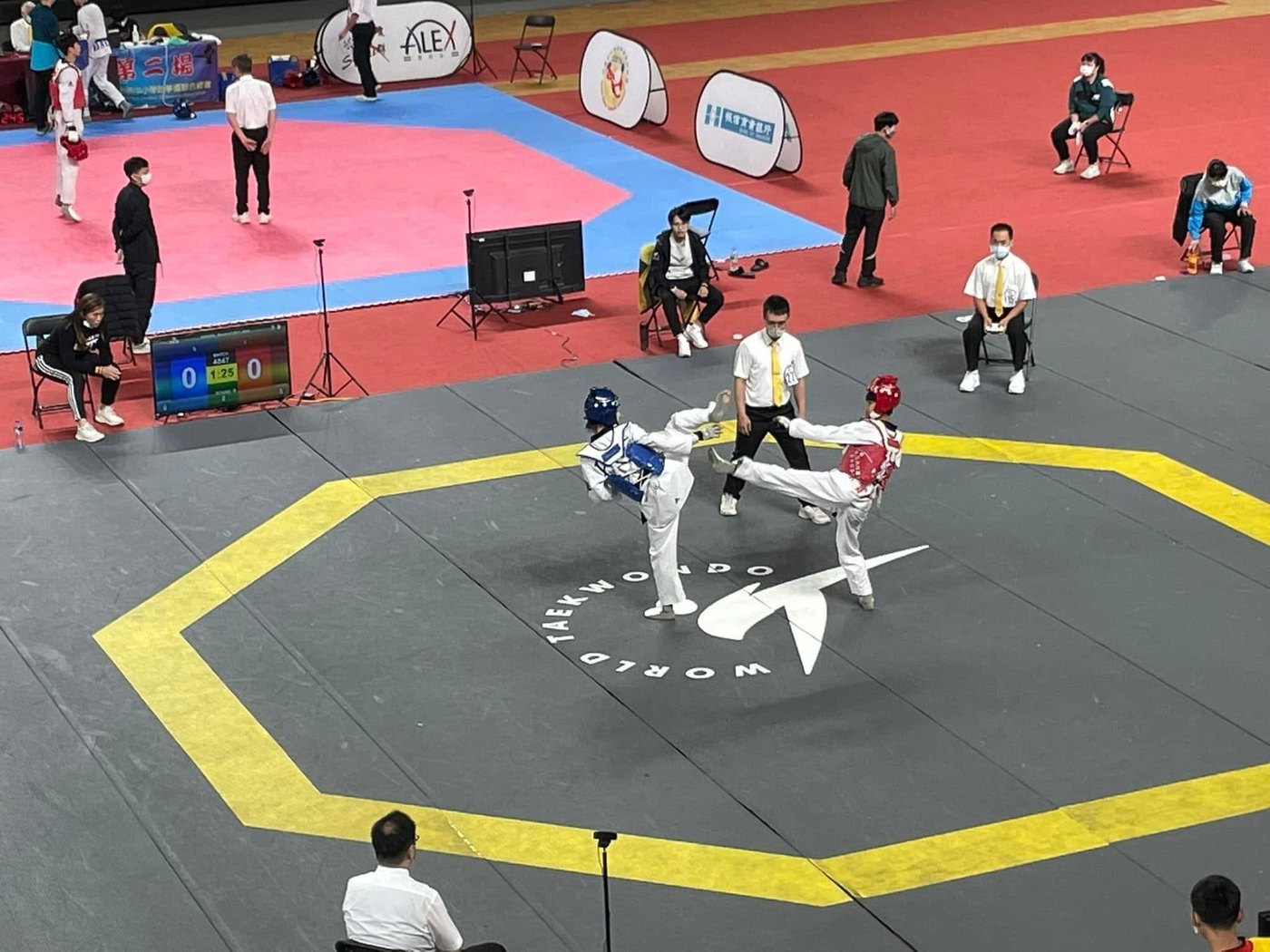 兩名選手在八角形比賽場地上對戰，裁判在旁，計分板顯示比數 Two competitors face each other on the octagonal contest area, a referee alongside and the scoreboard showing the score