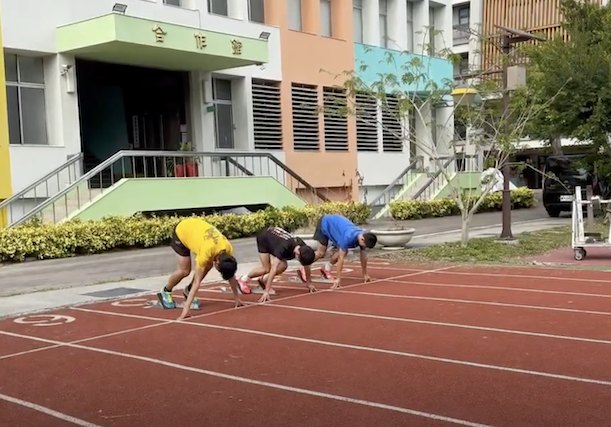 三名隊員在校內跑道上擺好起跑姿勢，雙手撐在起跑線上 Three team members set in the crouch start position on the school track, hands down on the line