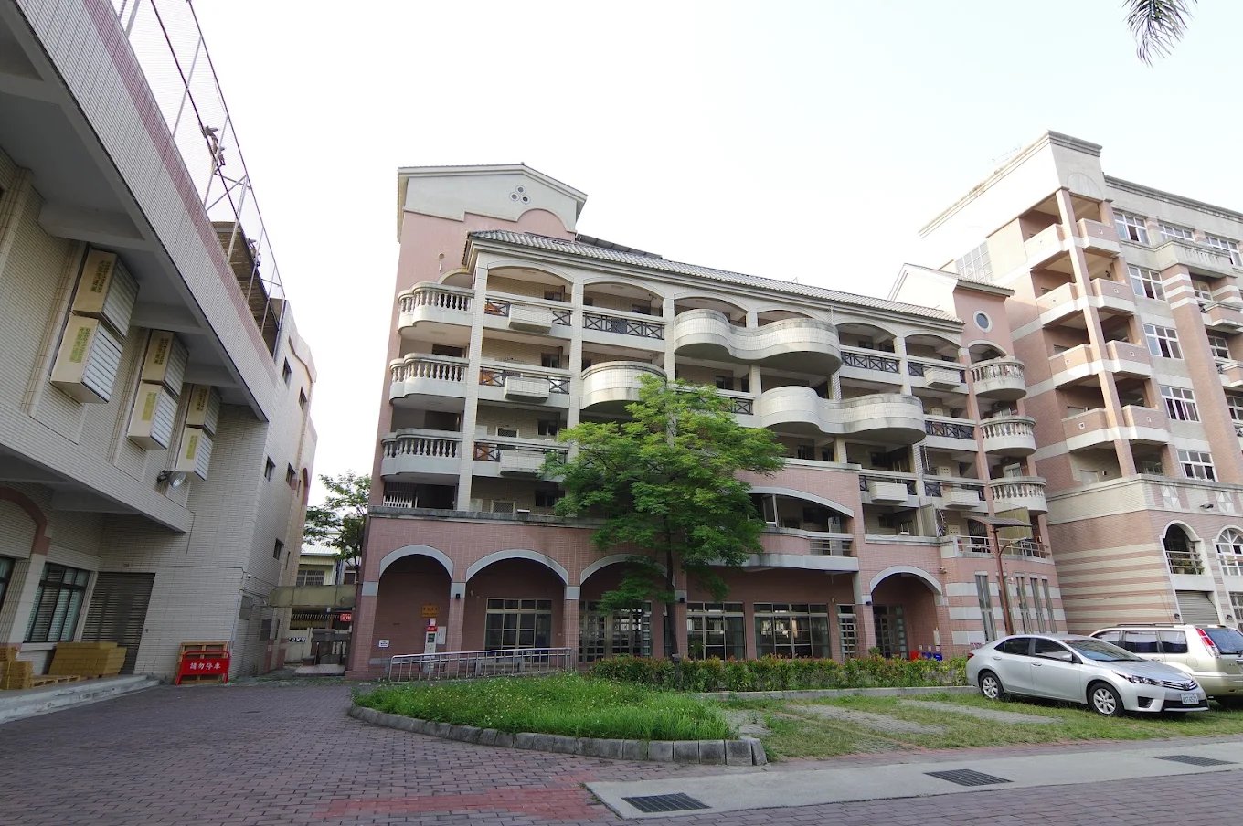 崇實高工的學生宿舍，粉色磚砌立面、拱門與層層陽台 The student dormitory at ChungShih, a pink brick façade with arched openings and tiers of balconies