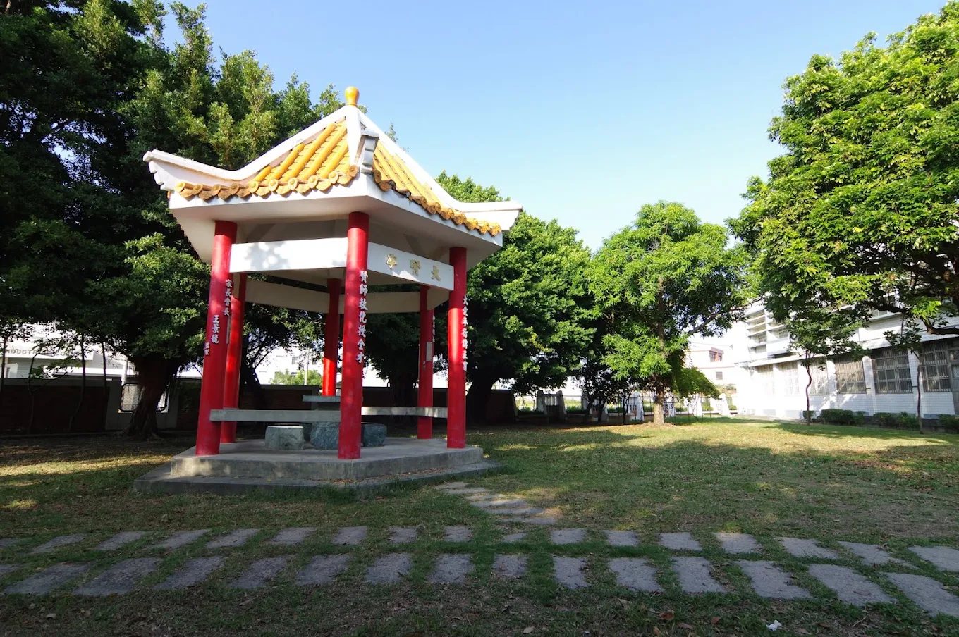 大嘉國小草地上的中式涼亭，紅色柱子與金黃琉璃瓦屋頂，前方是一條踏石小徑，藍天襯底 The Chinese-style pavilion on the Da Jah lawn — red pillars and a golden tiled roof, a stepping-stone path leading up to it against a blue sky