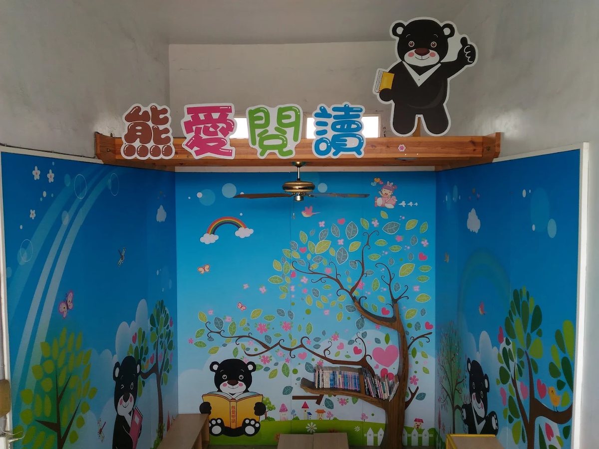 大嘉國小的熊愛閱讀角：藍色森林壁畫、彩虹與大樹，牆上「熊愛閱讀」四個彩色大字，一隻台灣黑熊立牌拿著書 The Bear Reading Corner at Da Jah — a blue forest mural with a rainbow and a big tree, the four colourful characters 熊愛閱讀 on the beam, and a Formosan black bear cut-out holding a book