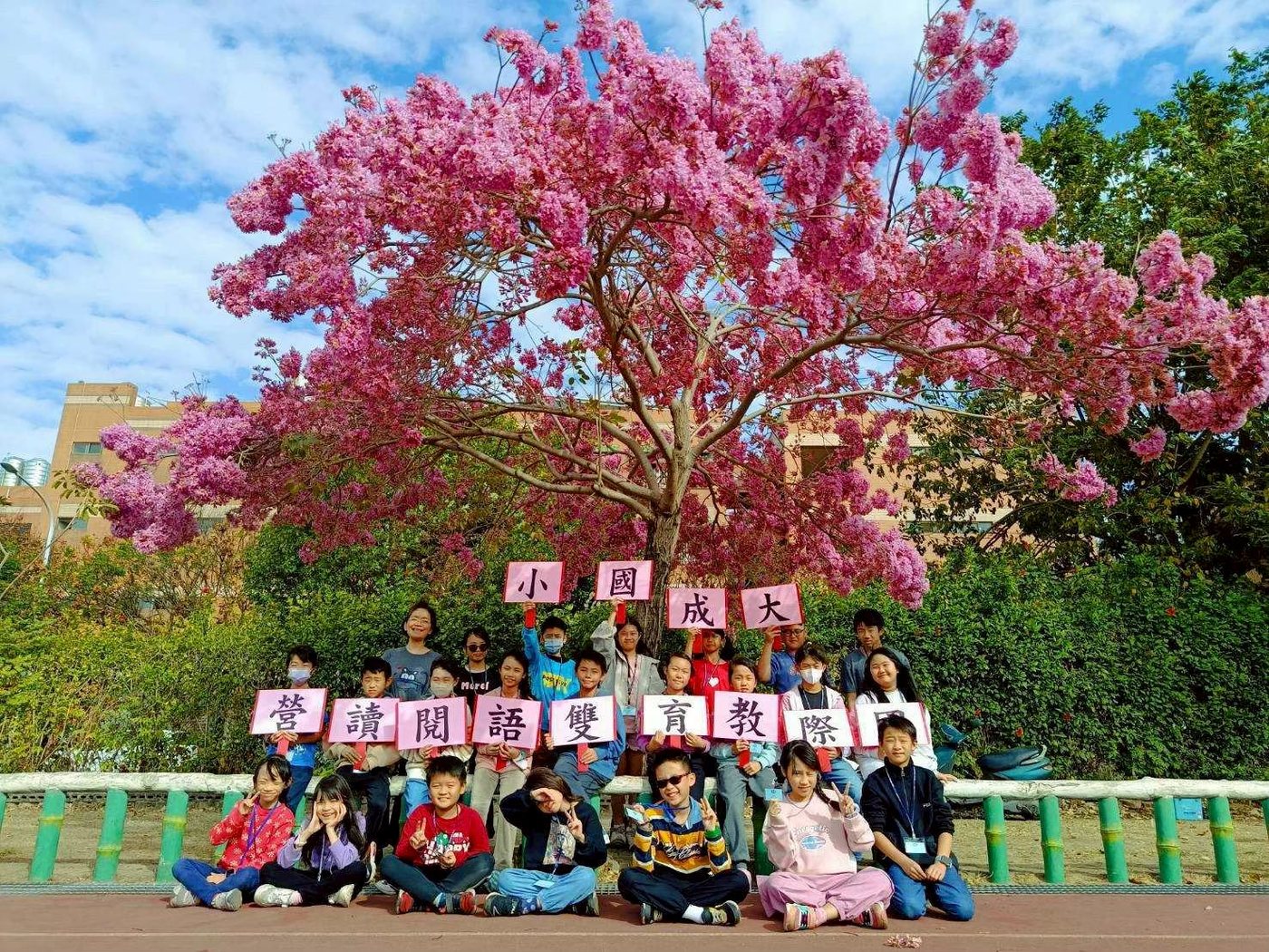 Students holding up character cards under a pink trumpet tree in bloom