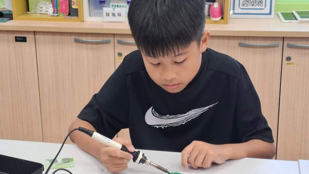 A student soldering a small circuit board in a maker classroom