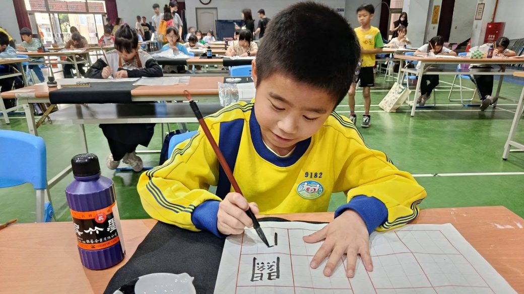 A student writing characters with brush and ink at a calligraphy contest