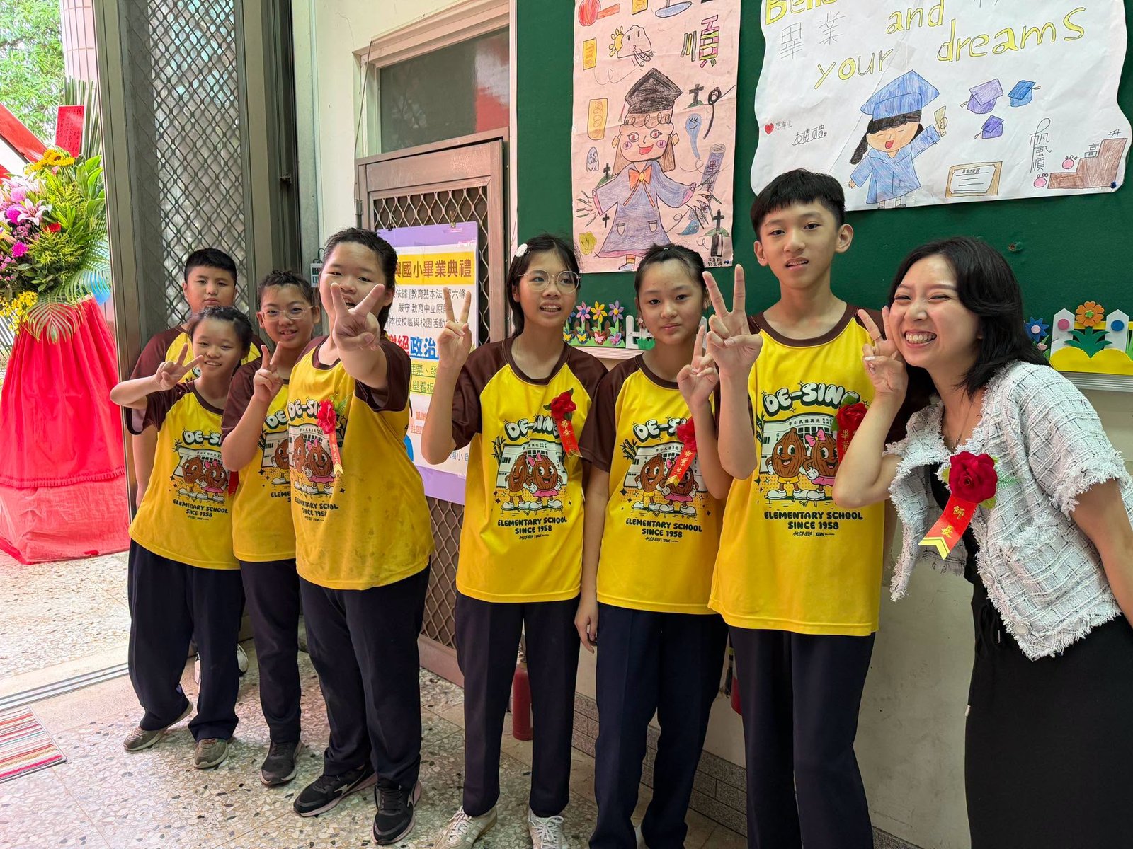 Graduates posing with their homeroom teacher by graduation artwork