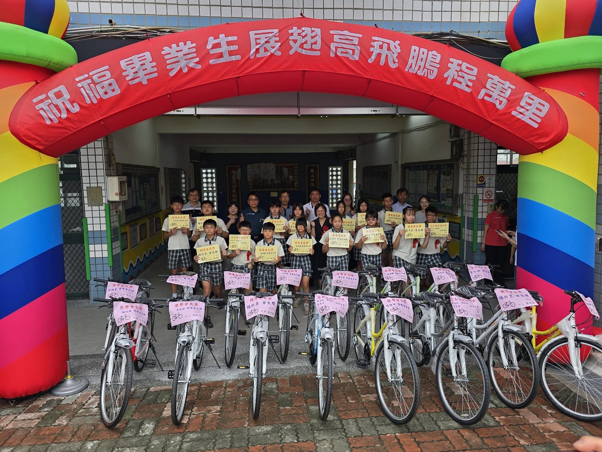 Graduates posing beneath a rainbow archway with donated bicycles