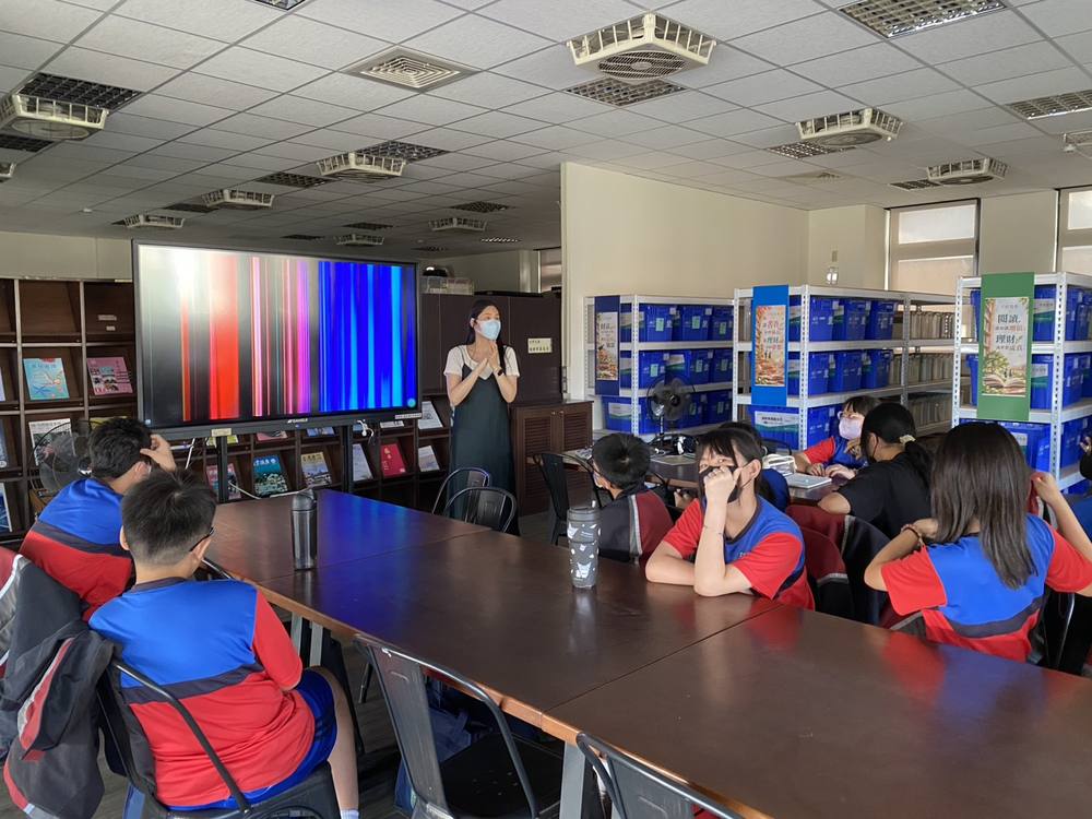 A teacher leads the drama club as students sit around long tables in the library