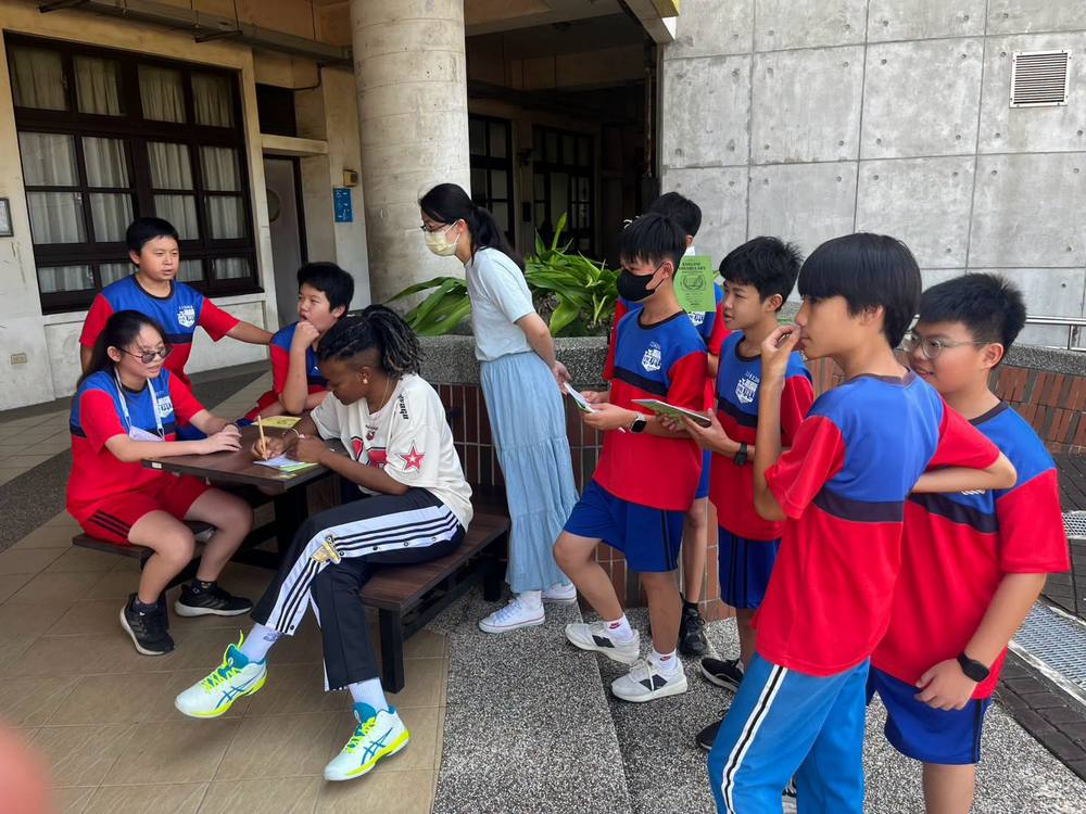 Students with vocabulary booklets gather around Teacher Z at an outdoor table