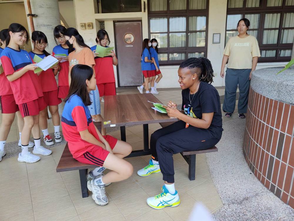 A student sits across from a smiling Teacher Z while classmates wait their turn
