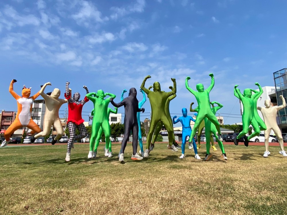 Students in colorful full-body Zentai suits leaping into the air on the school field