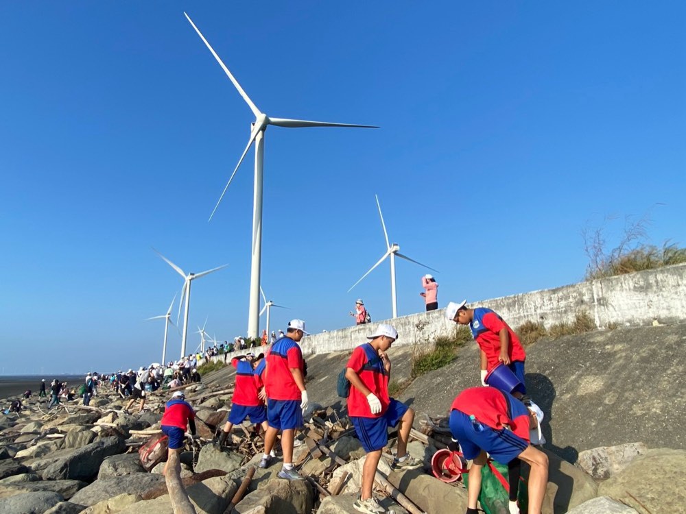 Students working their way along the rocky shore beneath a towering wind turbine