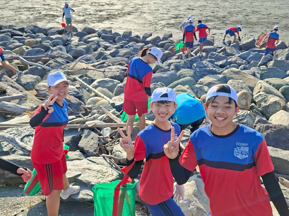 Smiling students flash peace signs on the rocks, green collection bags in hand