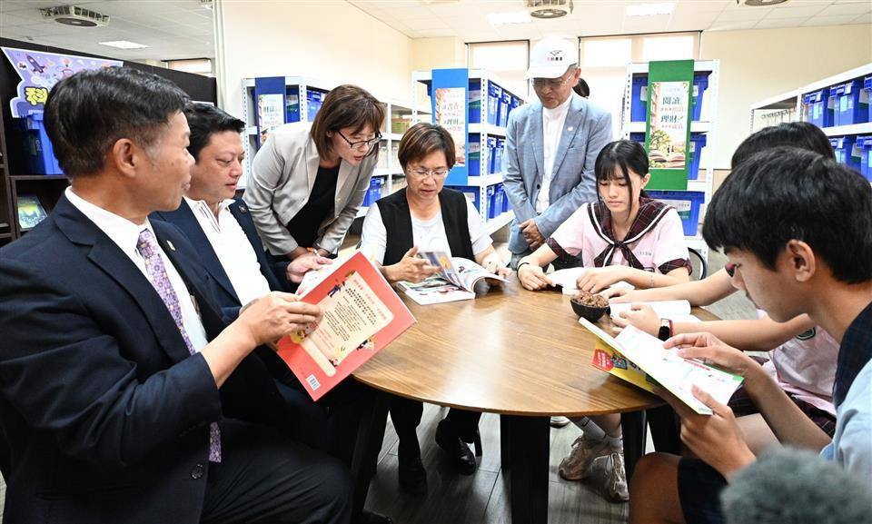 Guests sit at a round table and read new books together with students