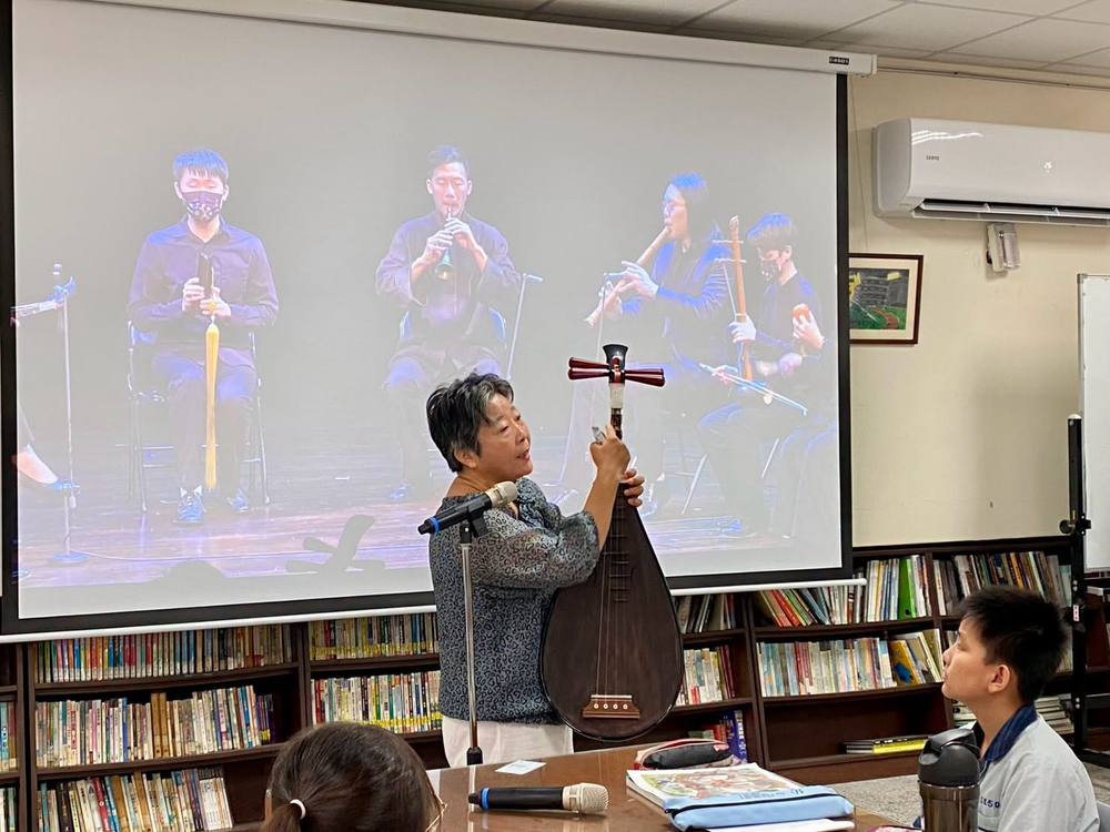 Teacher Wu holds up a pipa in front of a screen showing a Nanguan ensemble