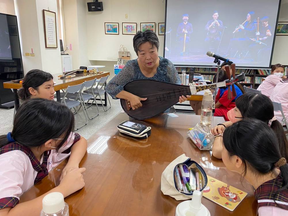 Teacher Wu plays the pipa at a table surrounded by students