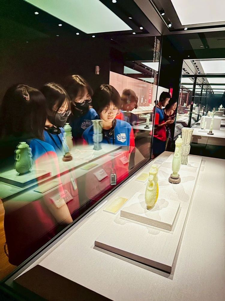 Students looking closely at a case of jade carvings reflected in the glass