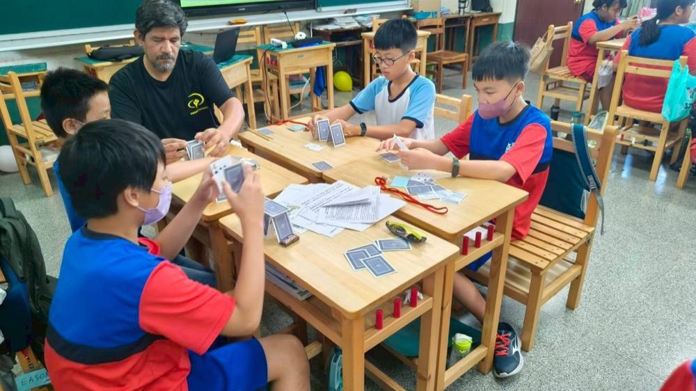 A foreign teacher playing a card game with students at their desks