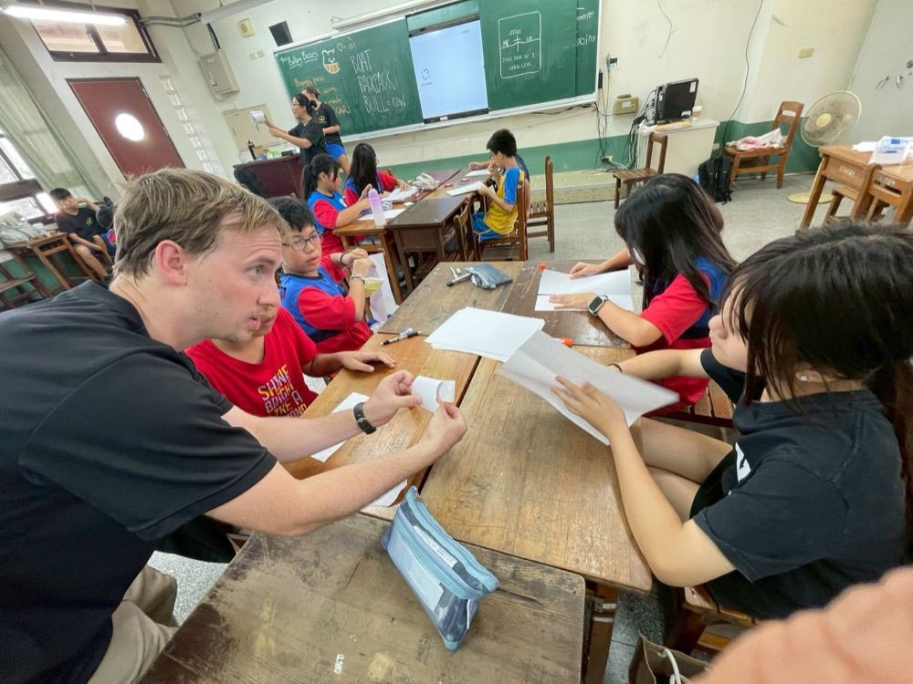 A foreign teacher working with students on a paper craft activity at their desks