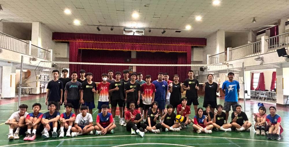 The volleyball team, returning graduates and Teacher Z pose together in the school gym