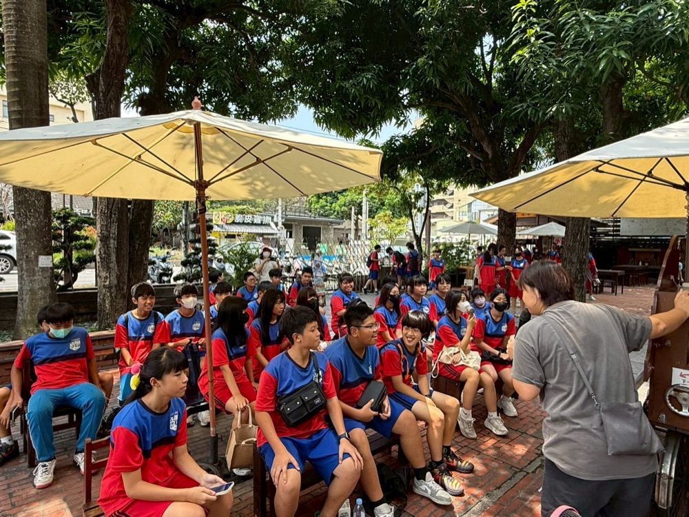 Students seated together outdoors under umbrellas at the Yunlin Story House