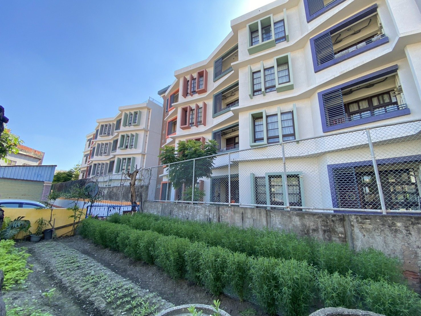 Garden classroom plots beside a colourful campus building · 校園食農教育園圃