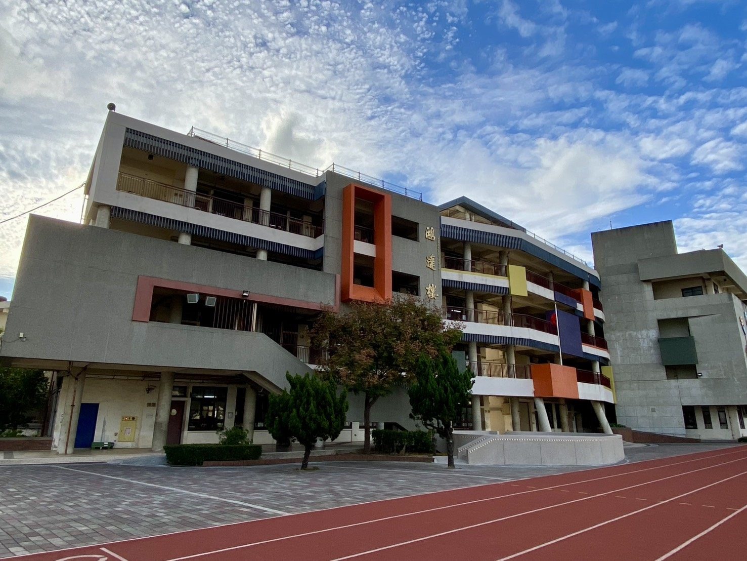 The colourful main teaching block under dramatic clouds · 尚毅樓教學主樓