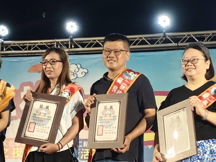 三位優良教師披著彩帶、手持獎狀在舞台上合影，中間為廣興國小昭安老師