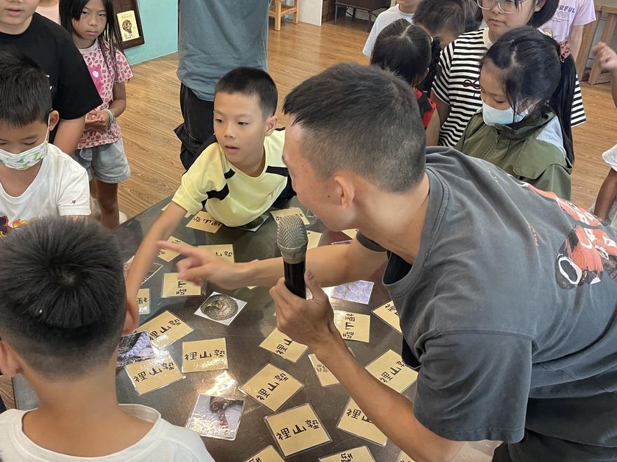 學生圍著桌子玩記憶卡牌遊戲，講師拿著麥克風蹲在旁邊引導