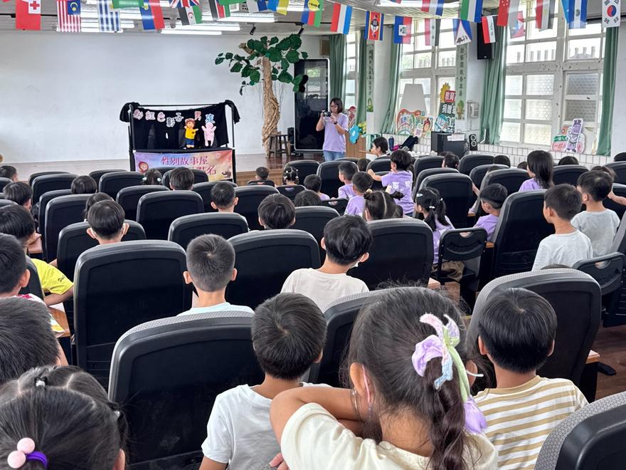 從禮堂後方看偶戲演出，幼兒園與國小學生坐在座位上專心觀賞