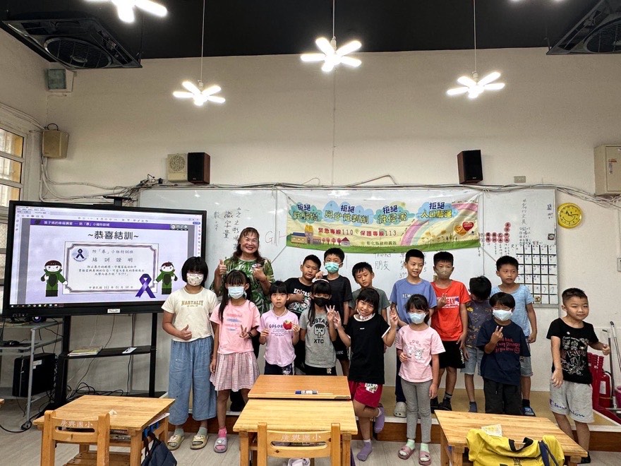 中低年級學生與講師在教室合影，背景布條寫著拒絕性騷擾、拒絕兒少性剝削、拒絕性侵害、拒絕人口販運