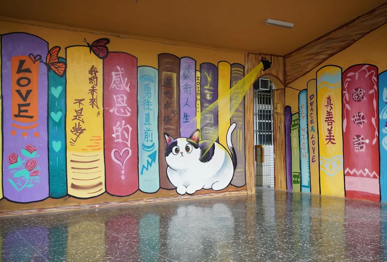 和美國小閱讀藝廊彩繪的書牆，畫著 LOVE、感恩的心、真善美等書名與一隻貓 A painted bookshelf wall in the reading gallery, its spines reading LOVE, gratitude and truth-goodness-beauty