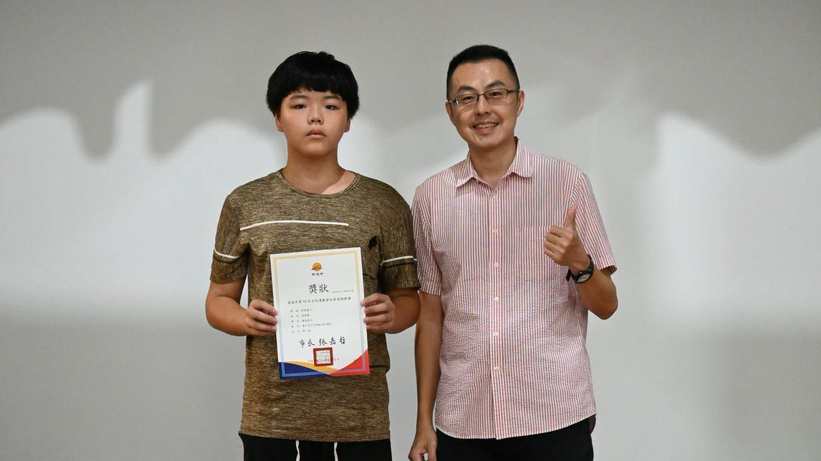 跆拳道冠軍同學手持南投市全民運動會跆拳道錦標賽獎狀與老師合影