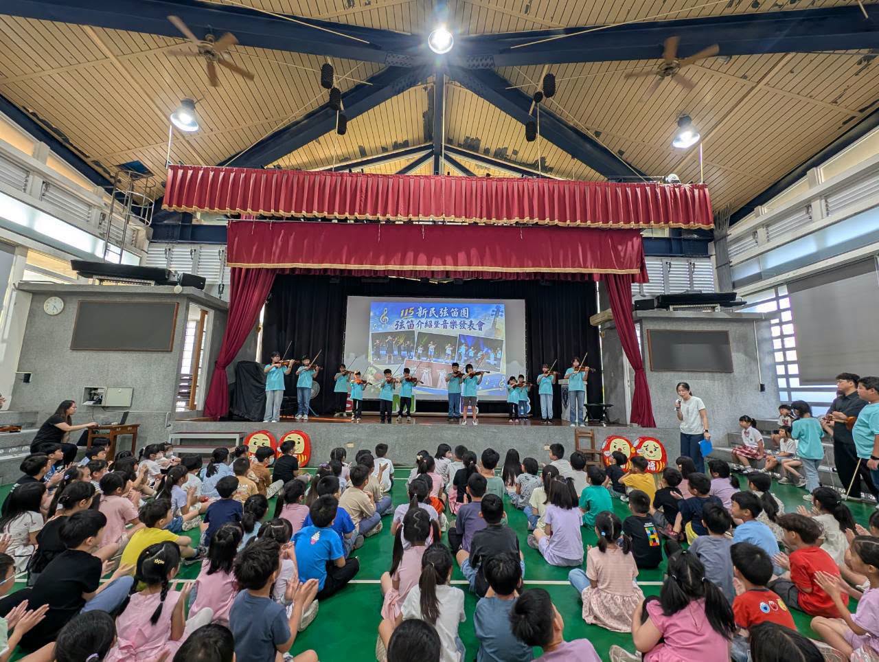集會堂裡弦樂團演出，一至三年級小朋友席地聆聽