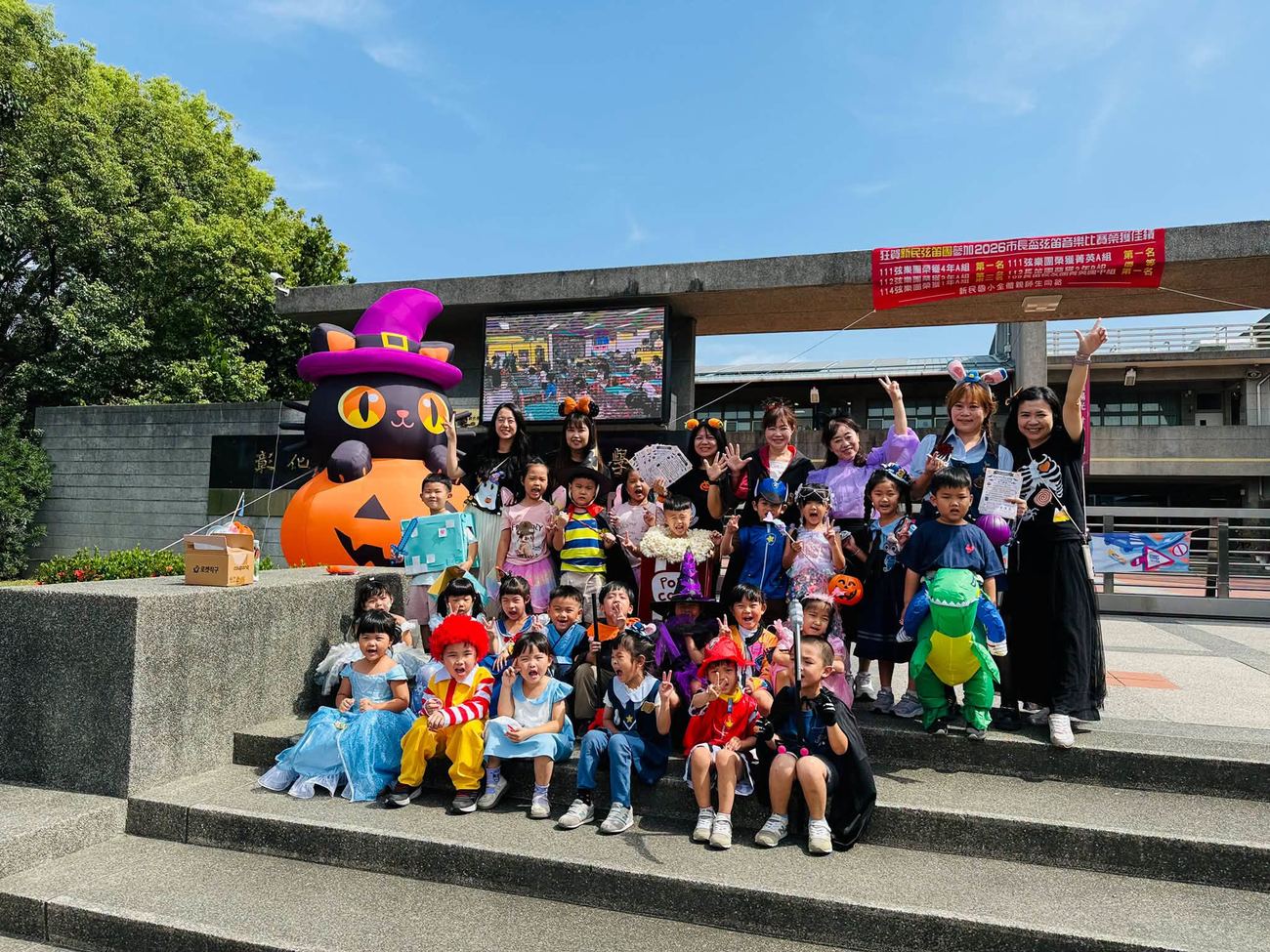 盛裝打扮的幼兒園小朋友與師長在新民校門口黑貓南瓜前大合照
