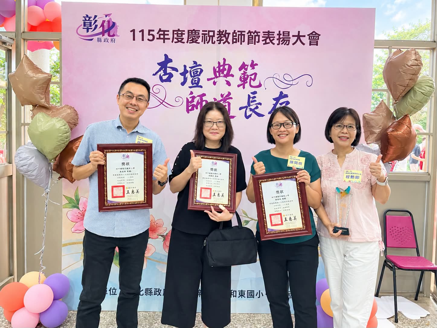新民國小四位夥伴在彰化縣教師節表揚大會上手持獎狀合影