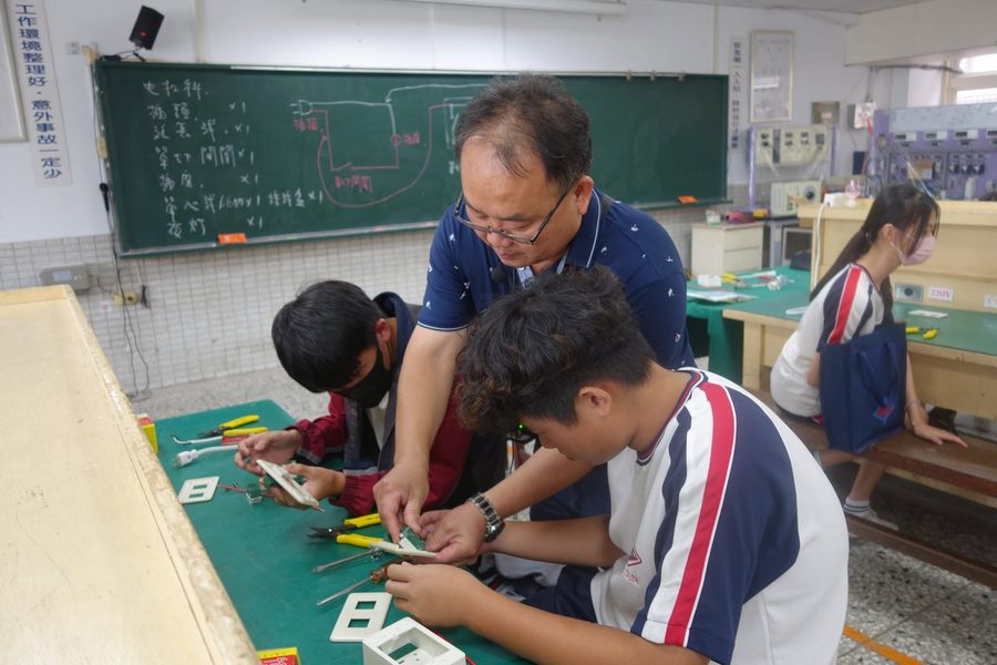老師在工場裡指導秀水國中學生練習電工配線 A teacher guiding Hsiushui students as they practice electrical wiring in a workshop
