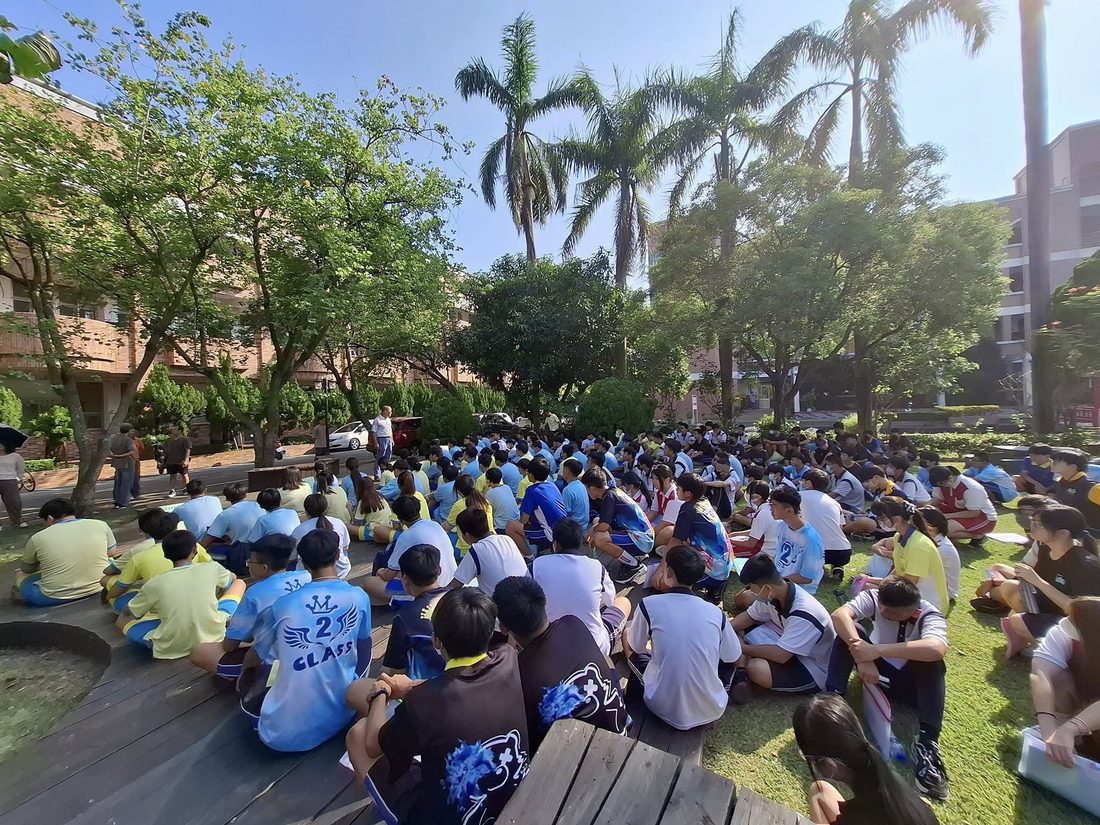 秀水國中學生坐在校園樹蔭下的草地上，一起參加活動 Hsiushui students sitting together on the lawn under the campus trees during an event