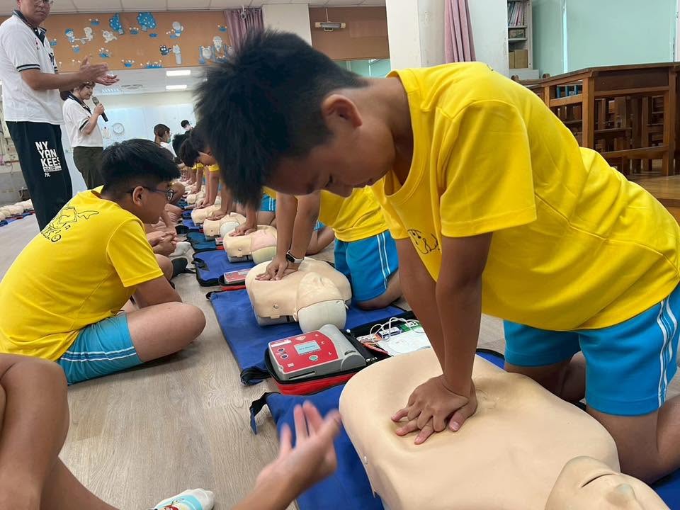 Students practicing chest compressions in a row, with an AED nearby