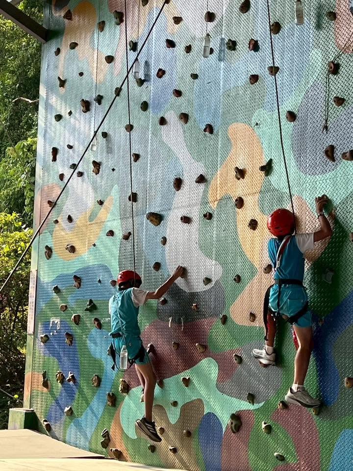 Two students in helmets rock climbing on an outdoor climbing wall