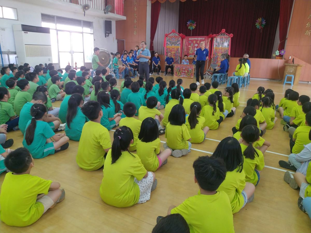 北管樂師在螺青國小體育館舞台上示範演出，學生席地而坐聆聽